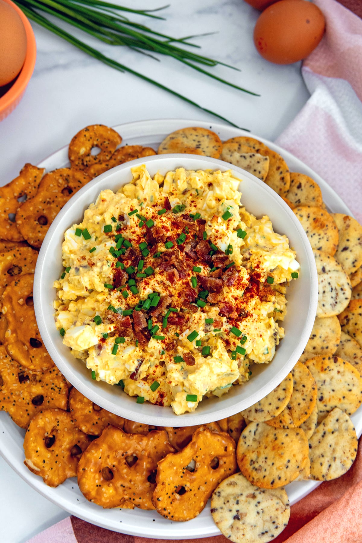 Close-up of creamy deviled egg dip garnished with crispy bacon and fresh chives, served with crackers